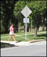 3 photos show the crosswalk; a woman holding a white cane on the ground in front of her walks to the street and puts one foot into the street, with the cane on the ground.